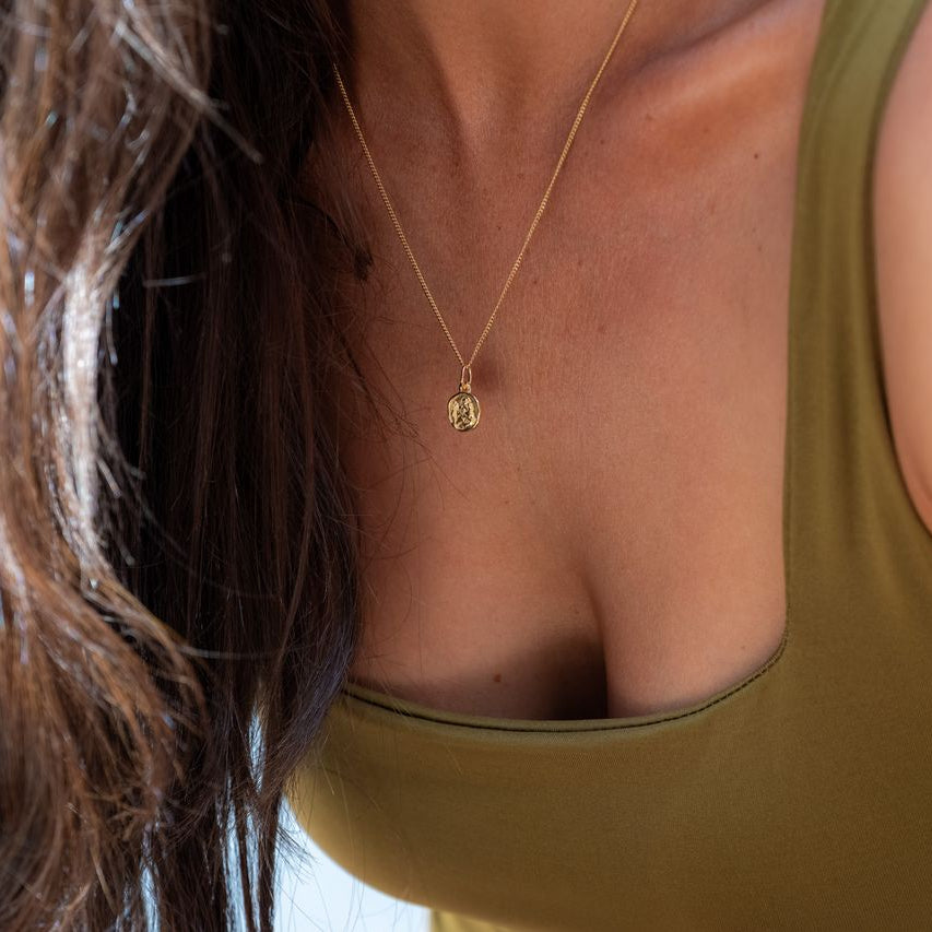 Woman wearing a fine chain necklace with a mini St. Christopher pendant