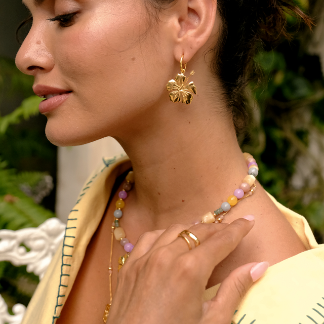 Woman wearing gold earrings and a necklace with a blurred green background by luna rose