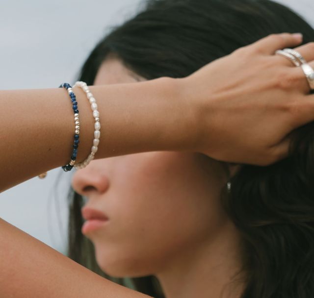 Sunlit beach scene featuring a woman wearing silver rings and bracelets paired with a pearl bracelet