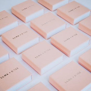 Rows of light pink jewelry boxes with "Luna and Rose" branding on a white surface.