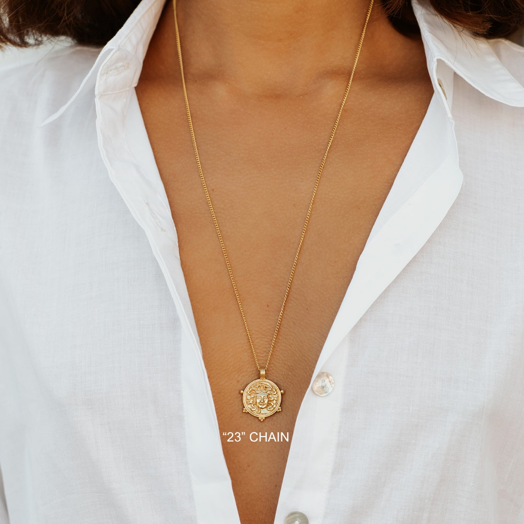 Gold necklace with a pendant on a person wearing a white shirt.