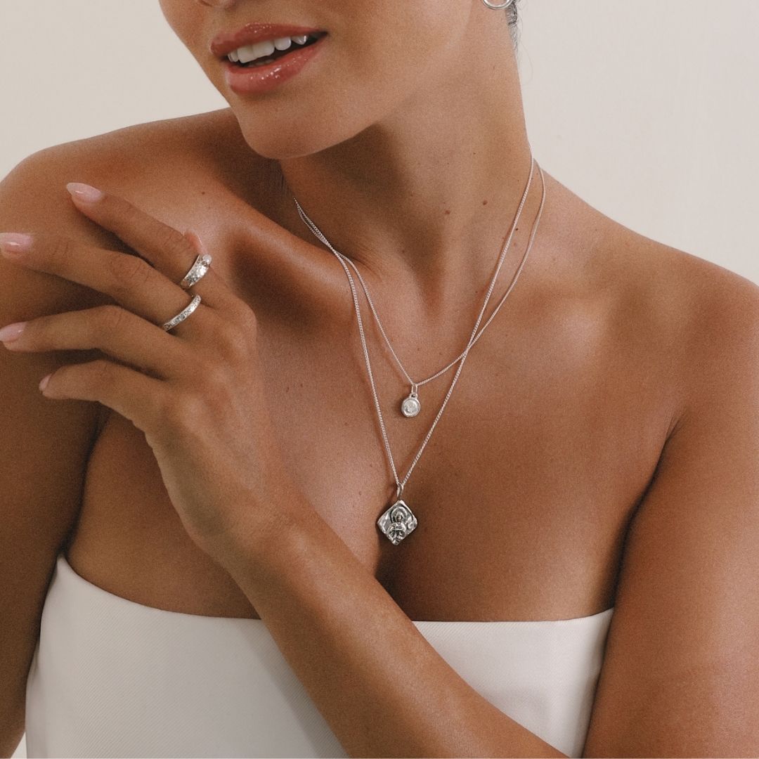 Woman wearing a silver necklace with a pendant, close-up on jewelry and skin.