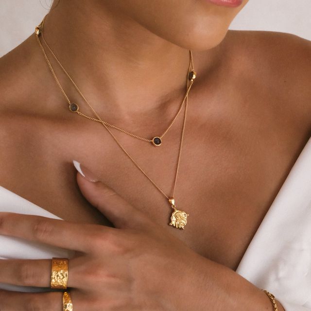 Fashion portrait of a woman wearing gold earrings, gemstone necklace, bracelet, and multiple gold rings