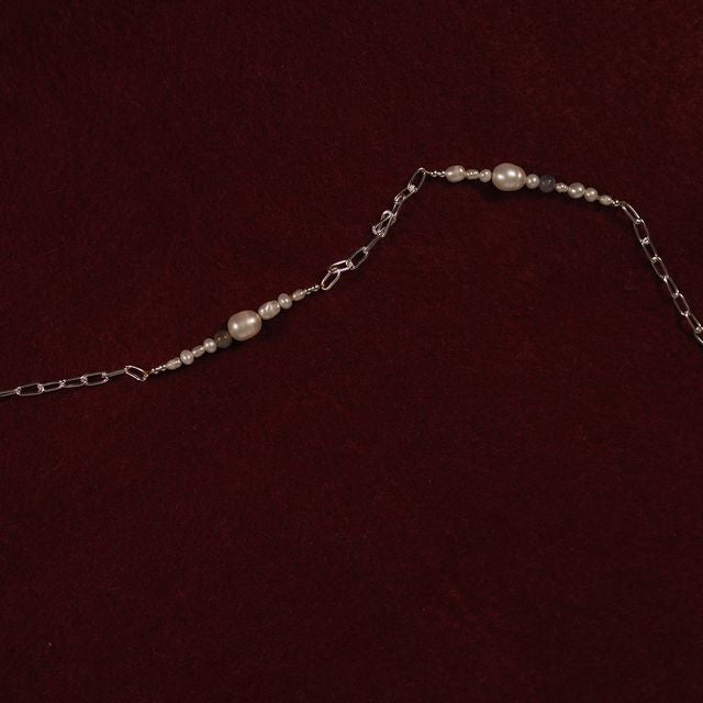 Minimalist display of a silver pearl necklace laid on red textile