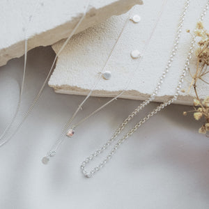 Silver chain necklace in three designs , displayed on beige stone with dried