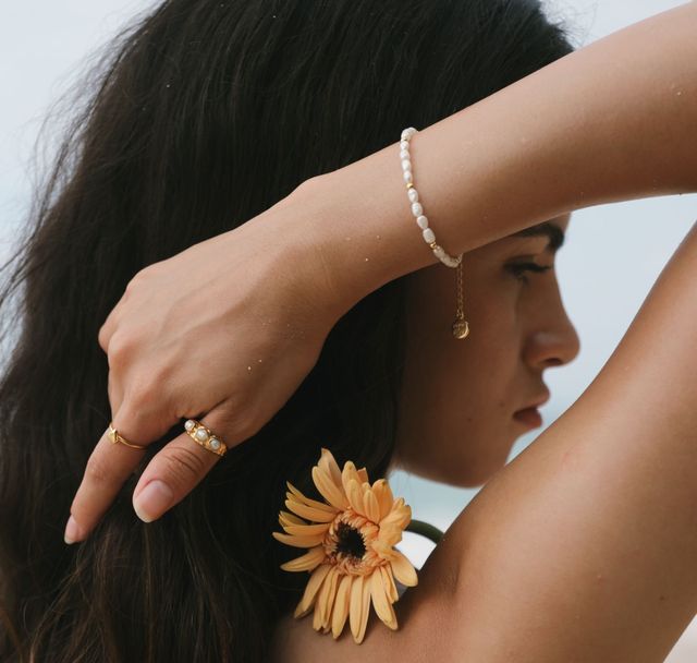 Woman with a floral accent, showcasing her pearl gold bracelet and matching multiple gold rings