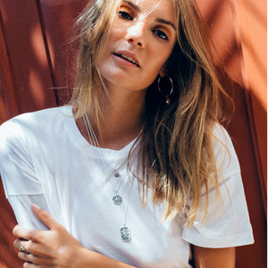 a woman with white tees wearing three layered  silver necklaces