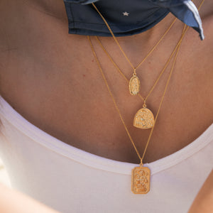 A person wearing three layered gold necklaces with various religious figure pendants and a blue scarf around the neck, against a light background.