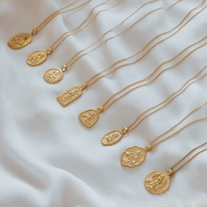 A collection of various gold pendant necklaces laid out on a soft white fabric.