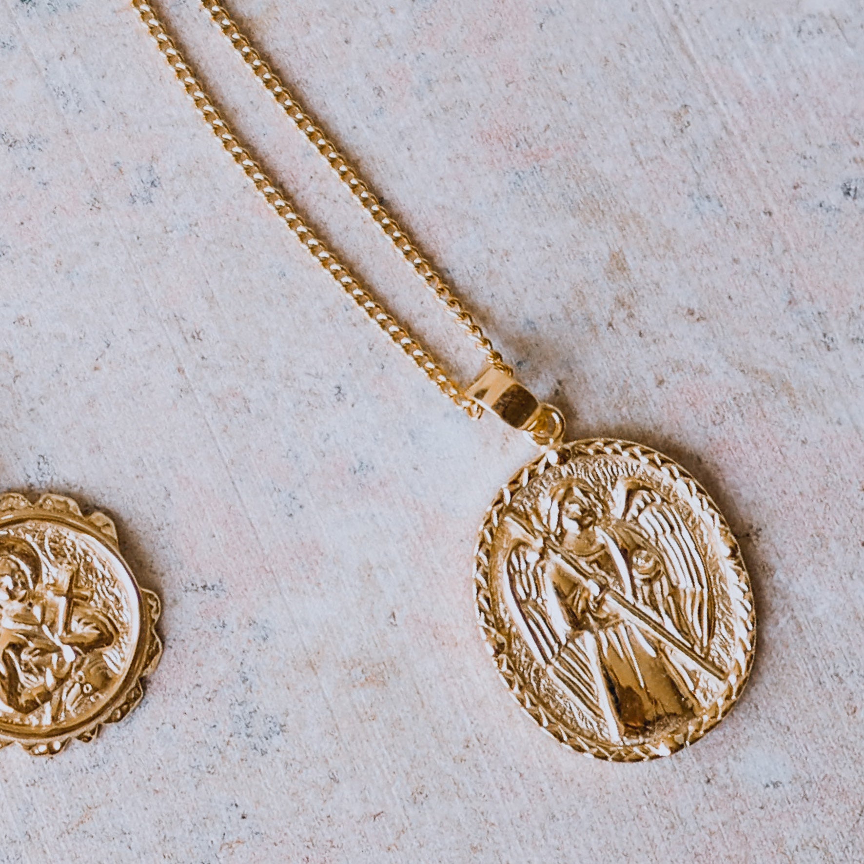 A gold necklace with an oval pendant featuring a raised religious figure design, displayed against a white background.